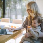 Woman Carrying her Baby and Working on a Laptop