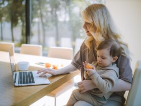 Woman Carrying her Baby and Working on a Laptop