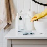 Person in glove wiping surface of sink in modern bathroom