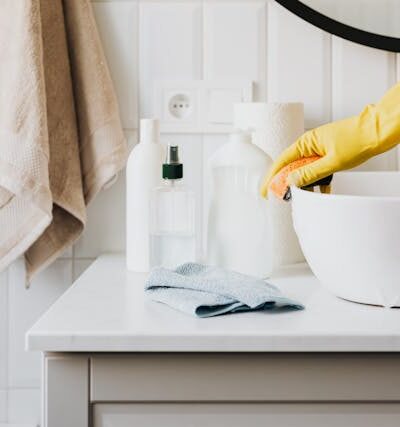 Person in glove wiping surface of sink in modern bathroom