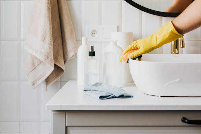 Person in glove wiping surface of sink in modern bathroom