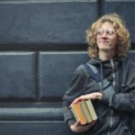 Man Leaning Against The Wall Holding A Books