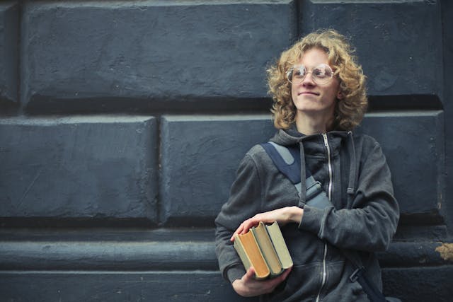 Man Leaning Against The Wall Holding A Books