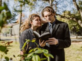 Man in Black Suit Jacket Reading a Bible Beside a Grieving Woman in Black Coat