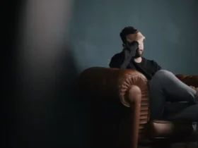 A man is sitting on a sofa with his hands on his head