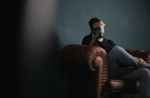 A man is sitting on a sofa with his hands on his head