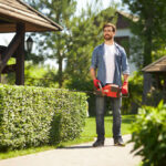 gardener standing carrying modern hand hedge trimmer in park