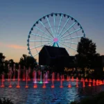 Ferris wheel and water fountain with colored lights at dusk