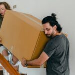 Concentrated couple carrying big carton box down stairs